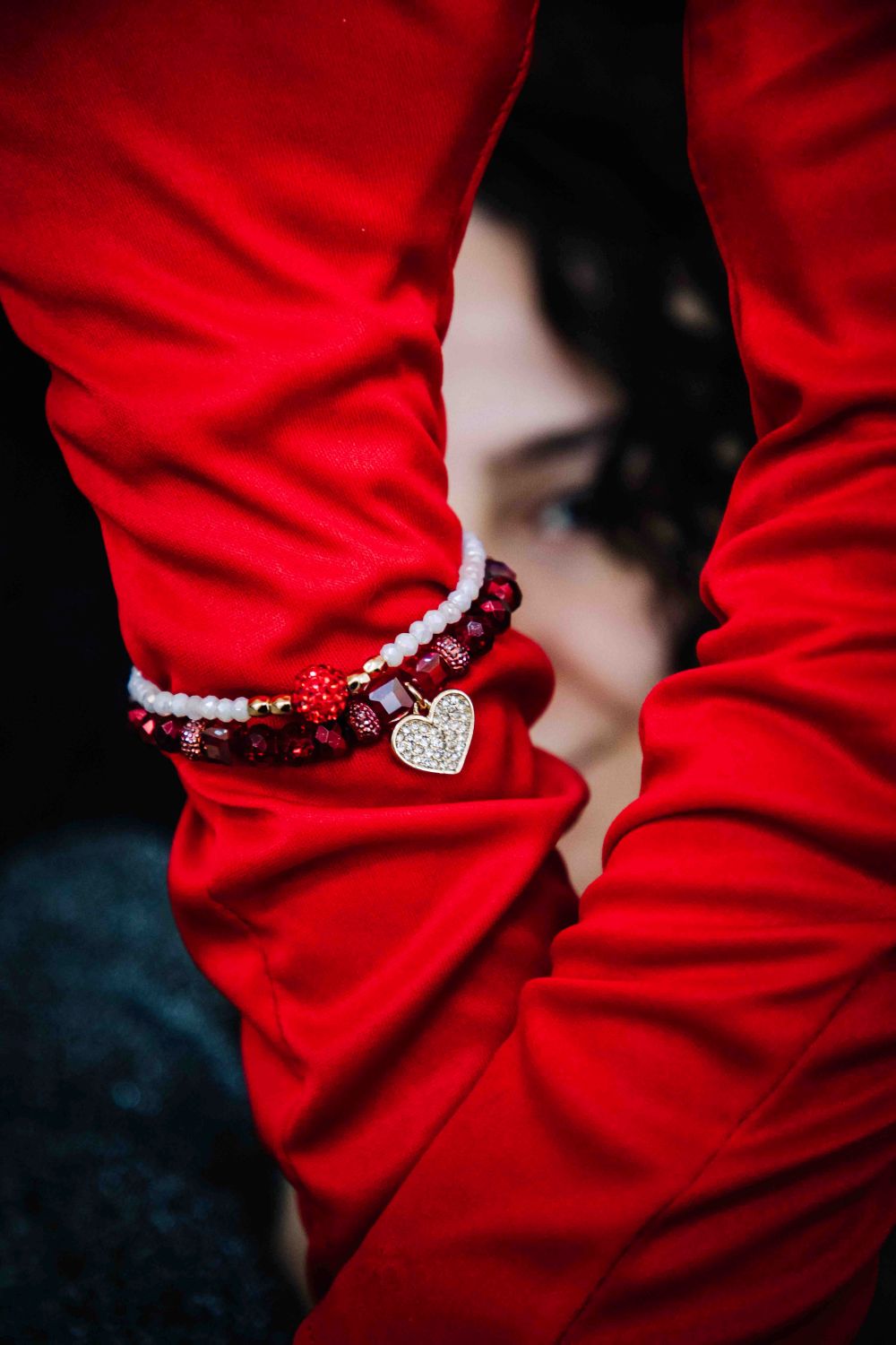 Close-up of a person wearing red pants with a bracelet featuring heart and star charms.