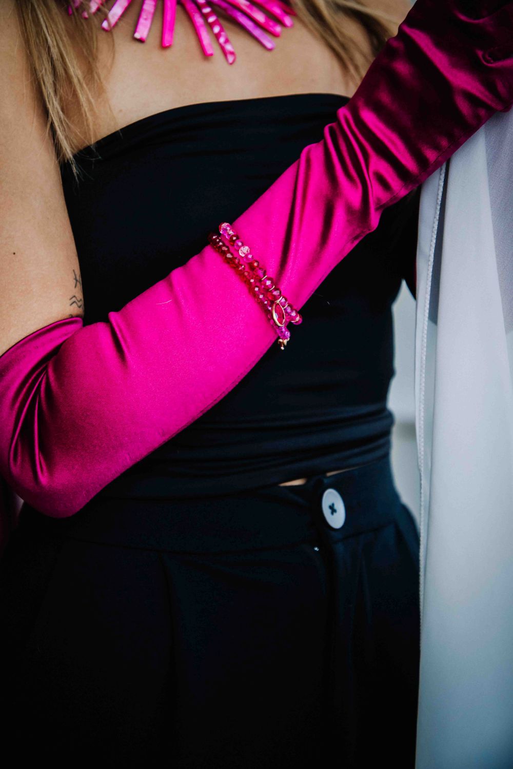 Person wearing a black top and bright pink satin gloves with decorative elements.