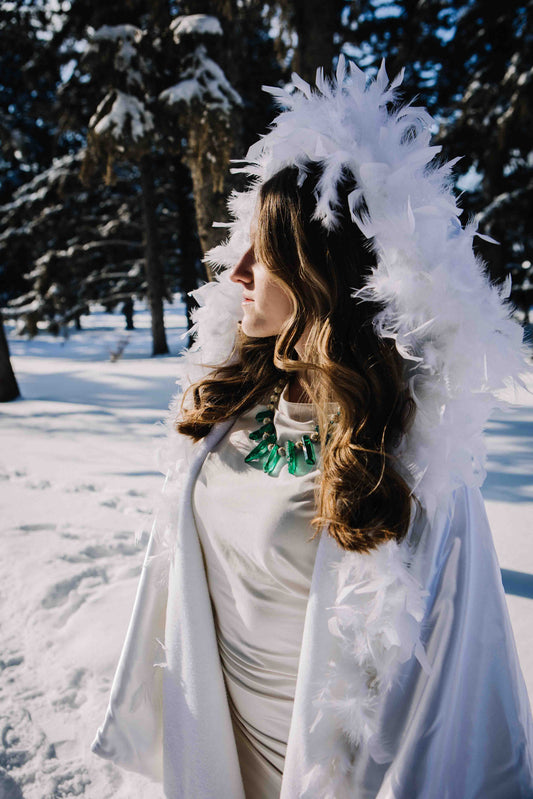 Person in a white feathered costume standing in a snowy forest