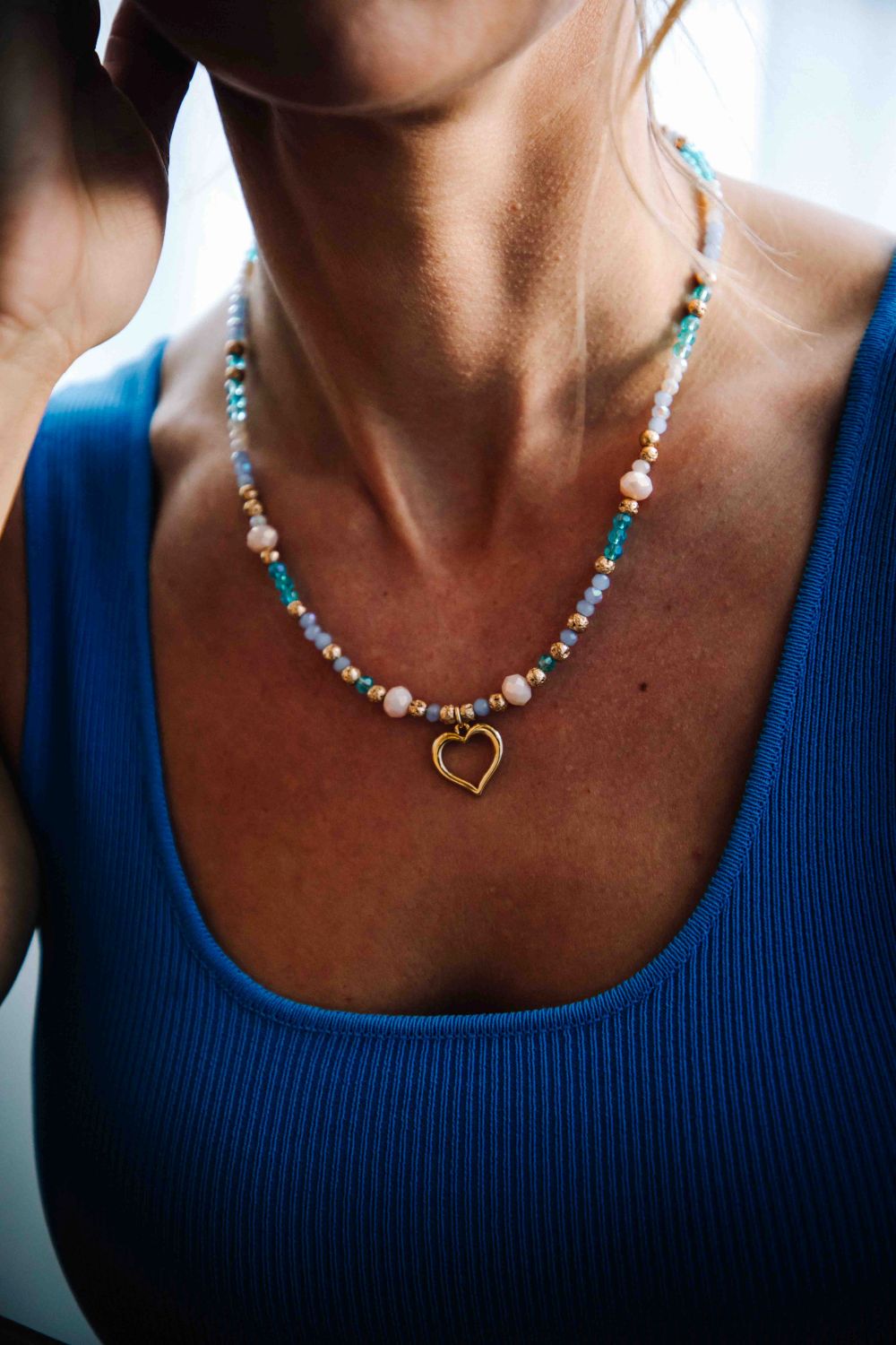 Necklace with a heart pendant worn by a person in a blue top.