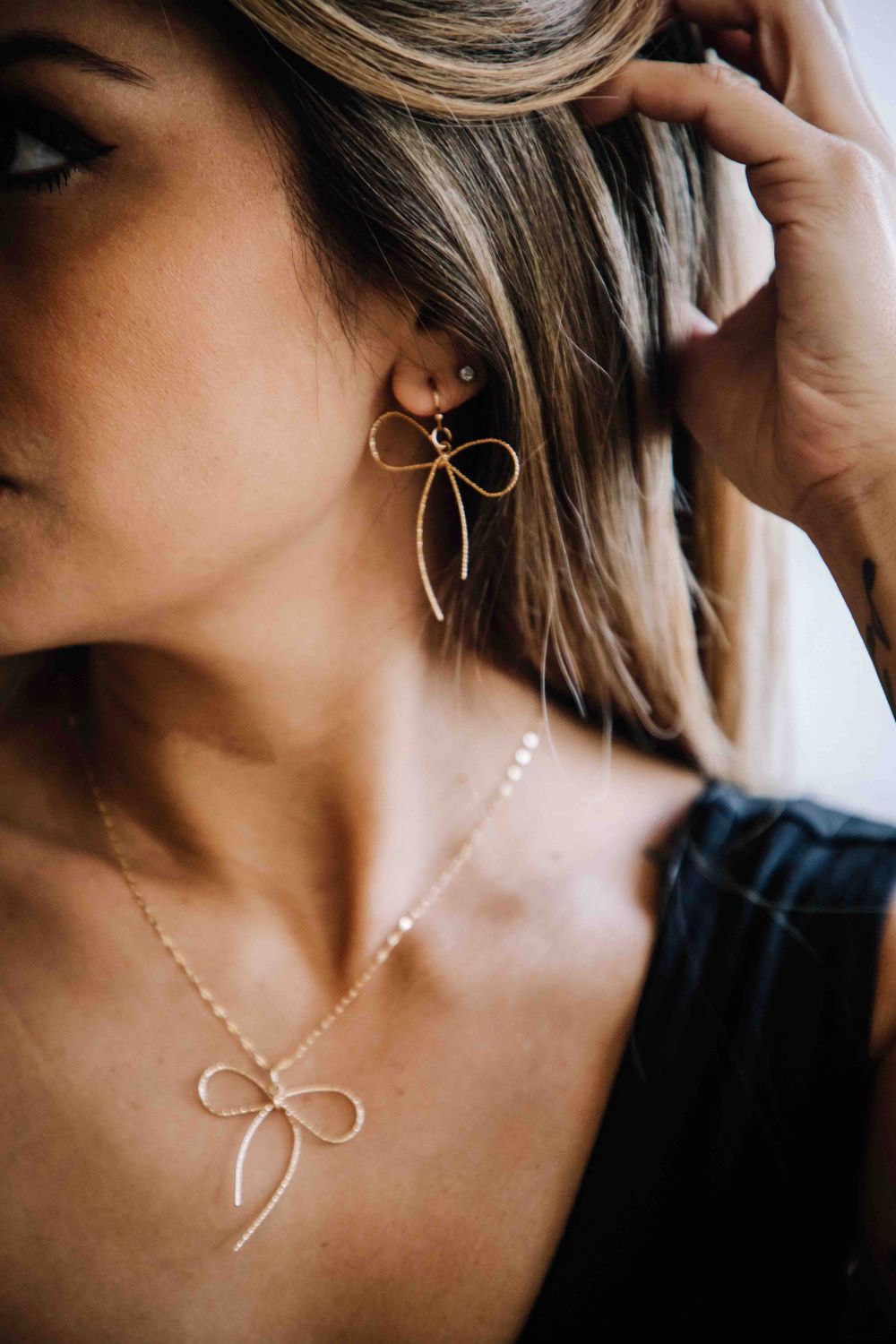 Close-up of a woman wearing gold bow-shaped earrings and necklace.