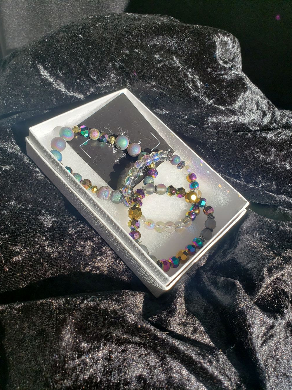 Colorful beaded bracelet in a white box with black background, placed on dark velvet fabric.