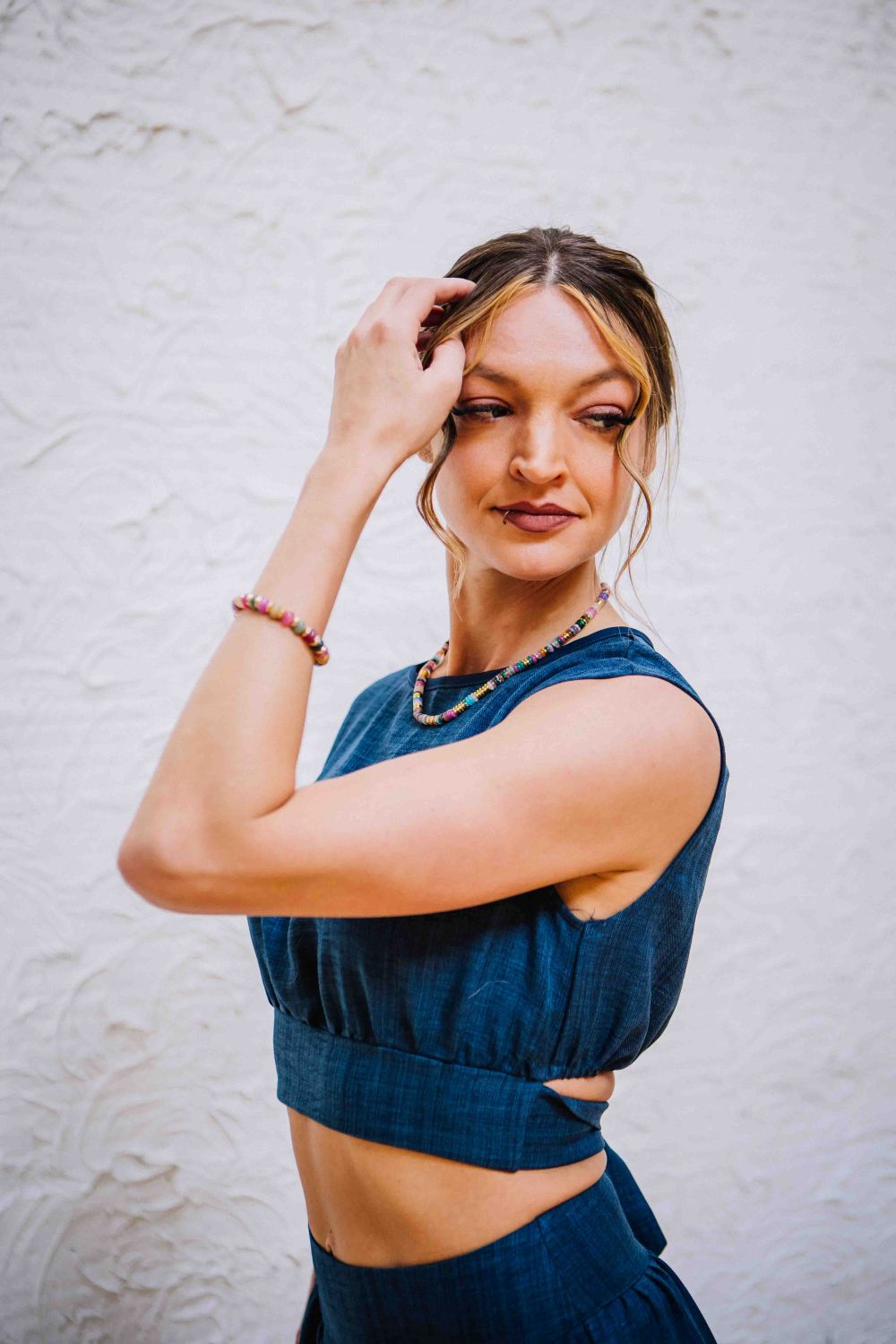 Woman wearing a blue sleeveless top and skirt against a light gray wall.