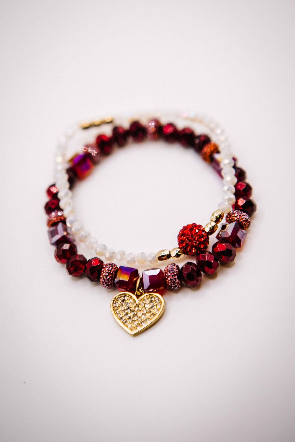 Bracelet with red beads and a gold heart charm on a white background