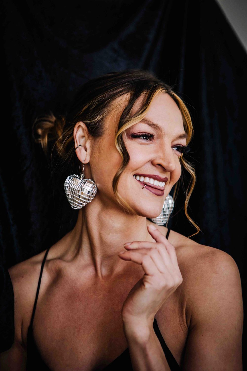 Woman wearing large heart-shaped earrings against a dark background