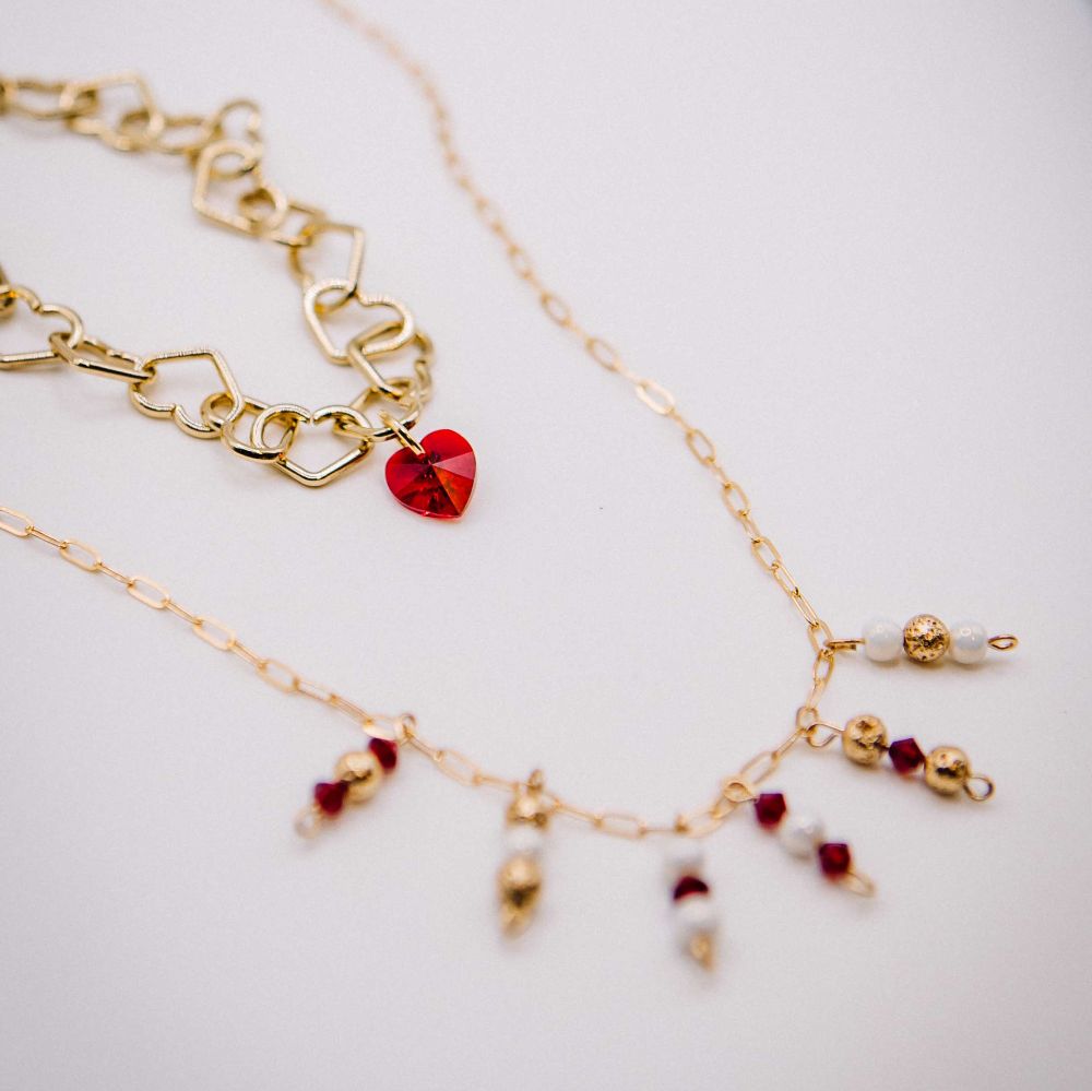 Gold necklaces with heart-shaped red pendant and beaded chain on a light background
