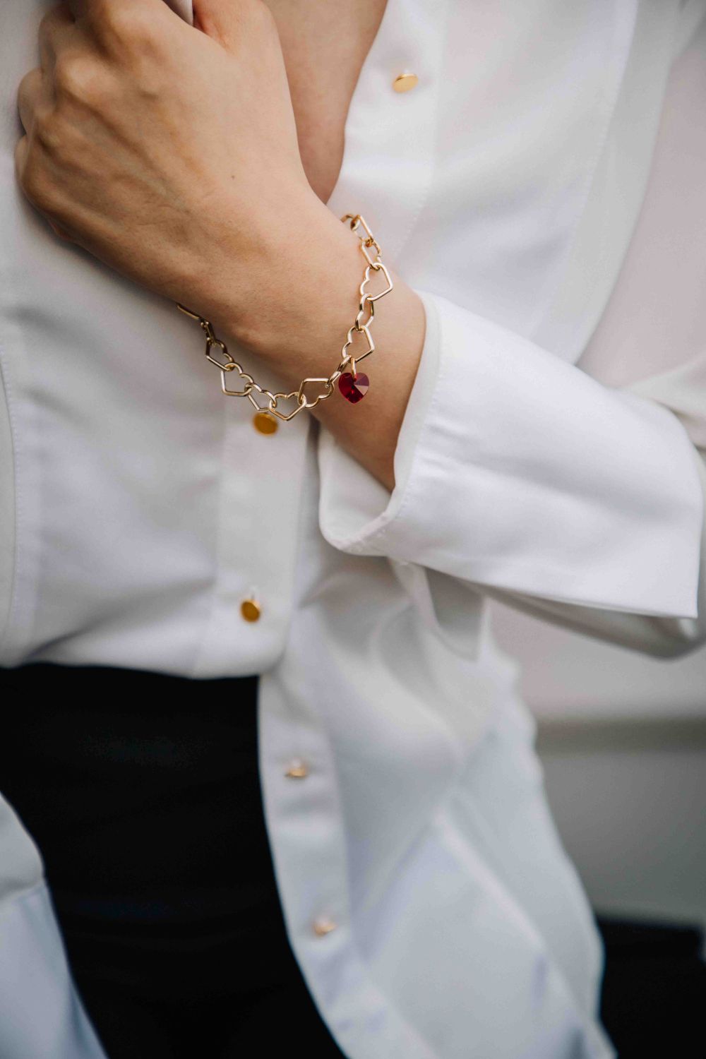 Close-up of a person wearing a gold bracelet with red gemstone on a white shirt.